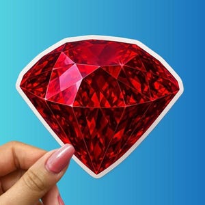 May include: A sticker featuring a large, faceted red gemstone with a white border. The gem is held by a hand with a pink nail polish against a blue background. The gem's facets reflect light.
