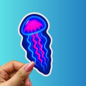 May include: A sticker featuring a vibrant jellyfish design. The jellyfish has a pink and blue color scheme, with a glowing effect. The sticker is held against a blue background.