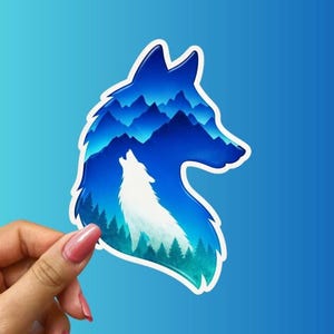 May include: A die-cut sticker shaped like a wolf head profile. The interior features a white silhouette of a howling wolf set against a gradient blue background of layered mountain peaks and a dense forest of pine trees at the base.