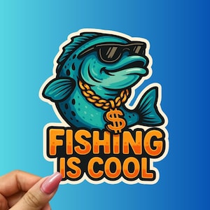 May include: A sticker featuring a cartoon fish wearing sunglasses and a gold chain with a dollar sign pendant. The fish is teal with black spots. The sticker has the text "FISHING IS COOL" in orange letters.
