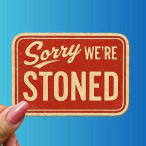 May include: A rectangular, red sign with rounded corners and the words "Sorry We're Stoned" in white, vintage-style lettering. The sign has a distressed, aged appearance, suggesting a retro or humorous theme. The background is a gradient of blue.