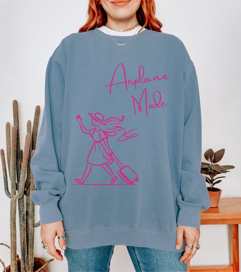 May include: A light blue sweatshirt with a pink graphic of a woman pulling a suitcase and the text "Airplane Mode".