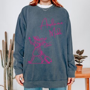 May include: A dark blue sweatshirt with a pink graphic of a woman carrying a suitcase and the text "Airplane Mode".