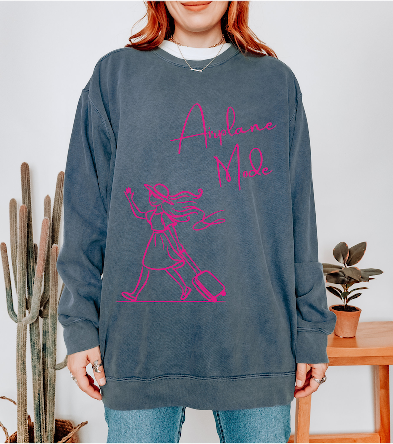 May include: A dark blue sweatshirt with a pink graphic of a woman carrying a suitcase and the text "Airplane Mode".