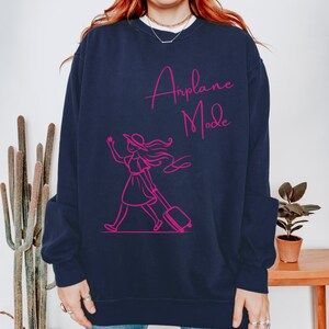 May include: A navy blue sweatshirt with a pink graphic of a woman walking with a suitcase and the text "Airplane Mode".
