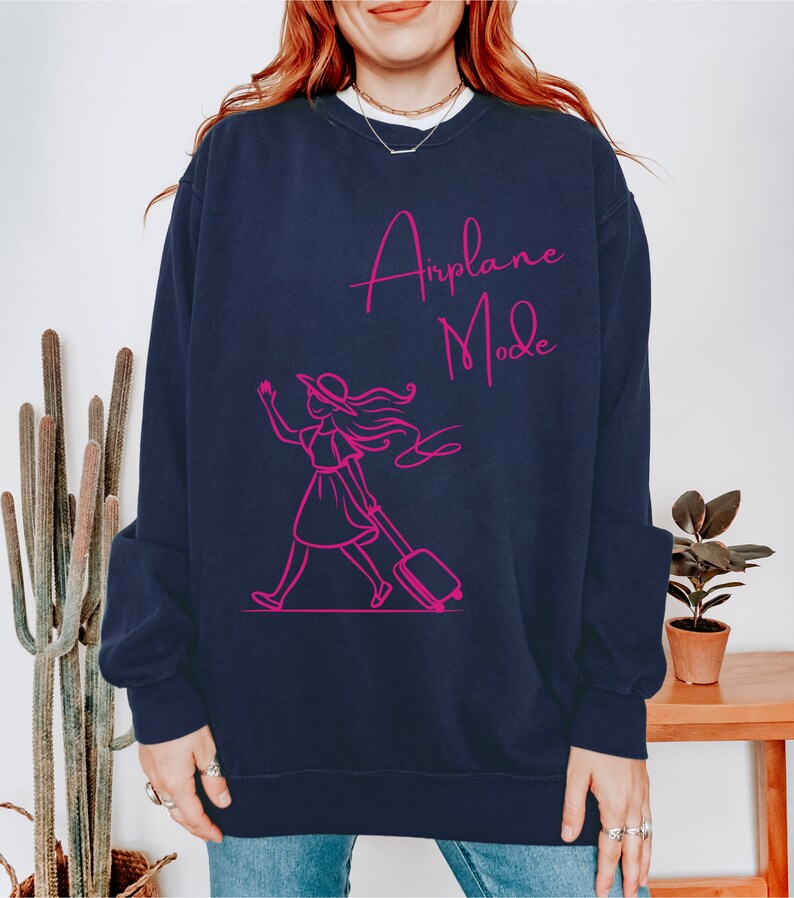 May include: A navy blue sweatshirt with a pink graphic of a woman walking with a suitcase and the text "Airplane Mode".