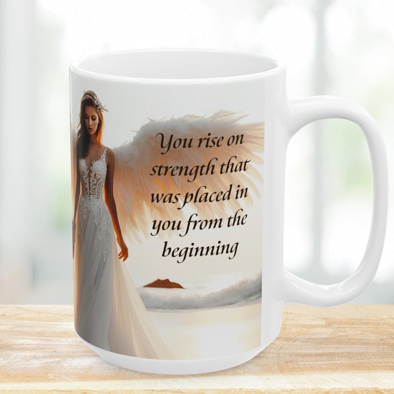Puede incluir: Taza de cer&aacute;mica blanca con una ilustraci&oacute;n de &aacute;ngel con grandes alas blancas y un vestido blanco fluido. La taza tiene el texto "You rise on strength that was placed in you from the beginning". La taza tiene un asa grande.