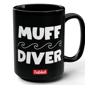 May include: Black ceramic coffee mug with white text that reads "MUFF DIVER" with a wavy line design underneath. The text "Table6" is printed in red at the bottom of the mug.