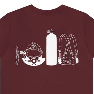 May include: A maroon t-shirt with a white graphic of a diving helmet, a scuba tank, a diving knife, and a diving harness.