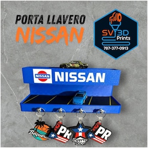 May include: A blue Nissan key holder with the Nissan logo and the text "Nissan". The key holder has a shelf with two toy cars and four keychains with Puerto Rican designs. The text "Porta Llavero" is above the Nissan logo.
