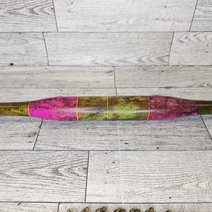 May include: A wooden rolling pin with a pink and green paint design. The rolling pin is approximately 45 cm long.