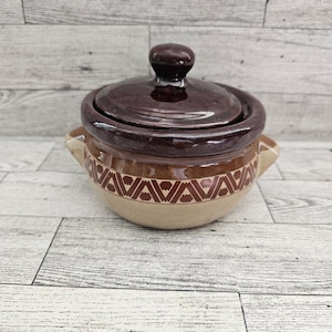 May include: A covered ceramic casserole dish. The lid and rim are a dark brown, while the body is tan with a repeating brown triangle pattern. The dish has two small handles and a rounded knob on the lid.