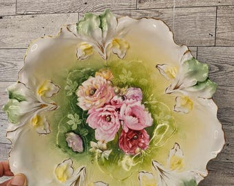 May include: A large, white porcelain bowl with a scalloped edge. The bowl is decorated with a floral design of pink and red roses, green leaves, and yellow accents. The bowl has a gold rim.