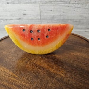 Puede incluir: Un objeto decorativo con forma de rebanada de sandía, hecho de mármol amarillo y rojo con semillas de mármol negro.