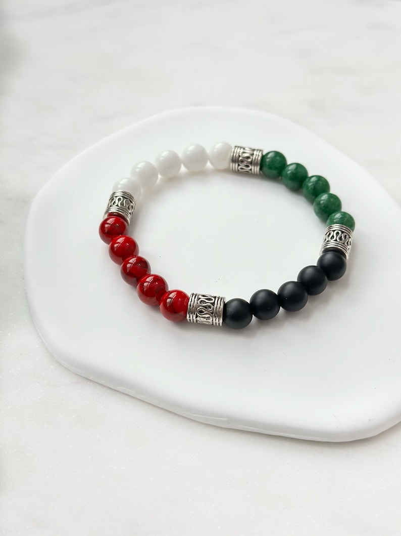May include: A bracelet with red, white, black, and green beads separated by silver spacers. The bracelet is on a white surface.