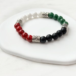 May include: A beaded bracelet with red, white, black, and green beads. The bracelet has silver accents.