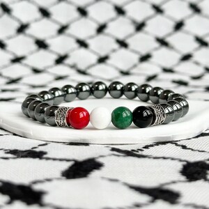 May include: A black hematite beaded bracelet with red, white, green, and black gemstone beads. The bracelet has silver accents.