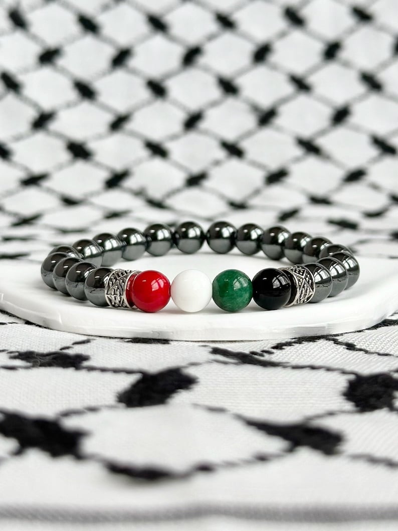 May include: A black hematite beaded bracelet with red, white, green, and black gemstone beads. The bracelet has silver accents.
