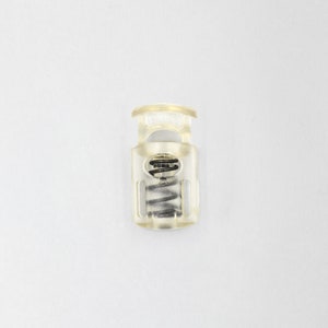 May include: A clear plastic toggle with a spring inside. The toggle is used for adjusting the length of cords or straps.