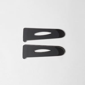 May include: Two black hair barrettes with a glossy finish, each featuring an oval cutout. The barrettes are positioned parallel against a white background, showcasing their sleek, minimalist design.