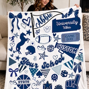 May include: A white fleece blanket with a navy blue and light blue design. The blanket features the name "Abbie", the words "University Vibes", "Game Day", and "Custom". It also includes various graphics like stars, hearts, and a football.