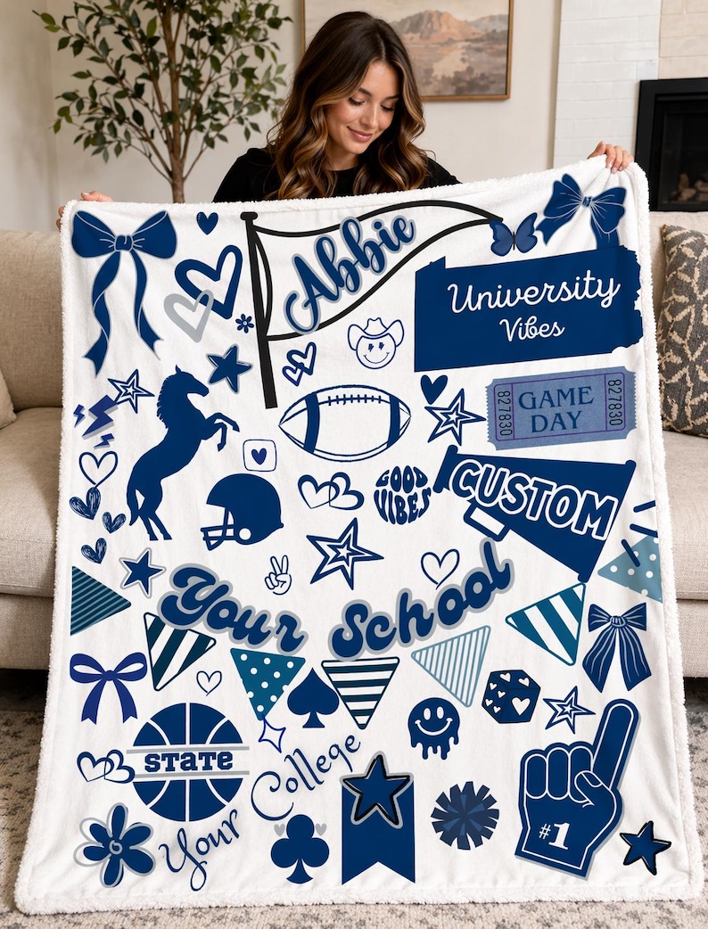 May include: A white fleece blanket with a navy blue and light blue design. The blanket features the name "Abbie", the words "University Vibes", "Game Day", and "Custom". It also includes various graphics like stars, hearts, and a football.