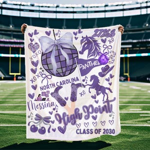 May include: A white blanket with purple graphics, including a disco ball, horses, cowboy boots, and hearts. Text includes "North Carolina," "High Point," and "Class of 2030." The blanket is held up against a green field.