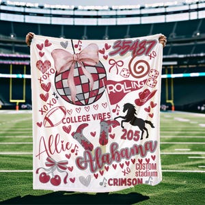 May include: A white blanket with a design featuring a disco ball, hearts, and the text "Alabama". The design includes a football, cowboy boots, and the words "College Vibes". The blanket is held up in front of a football stadium.