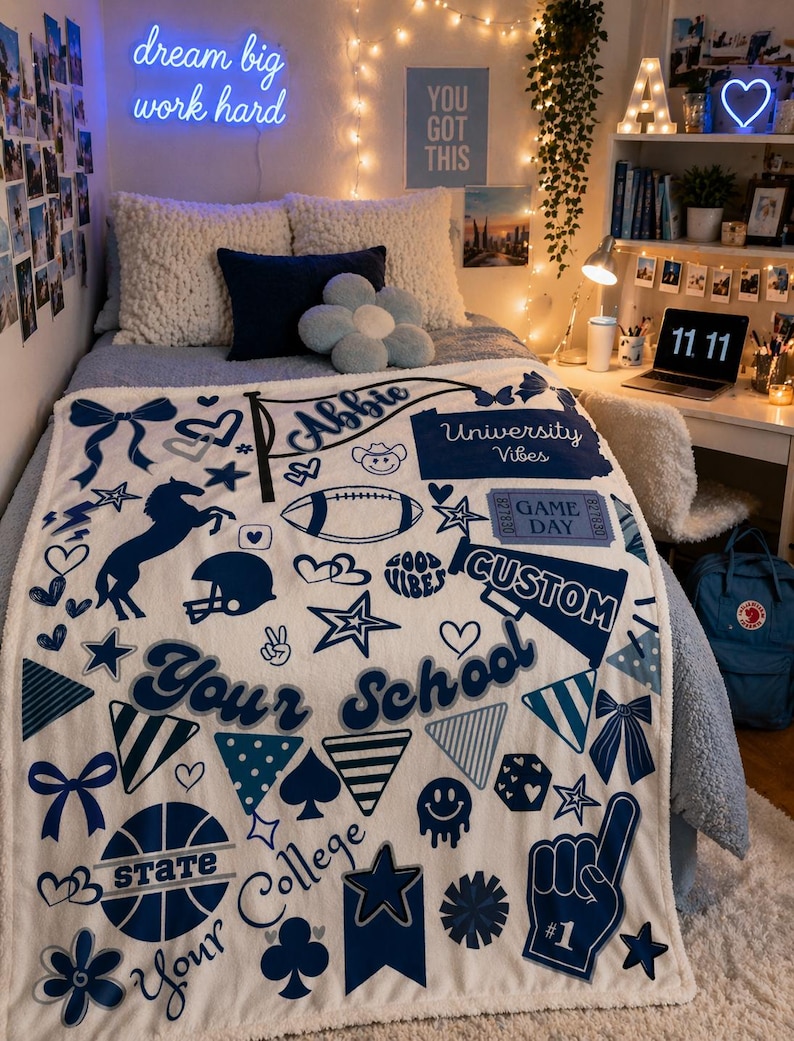 May include: A white and blue custom blanket with various graphics, including a football, stars, and the text "Your School." The blanket also features the name "Abbie" and the phrases "University Vibes" and "Game Day."