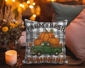 May include: Square pillow with a black and white checkered pattern. The pillow features a green truck carrying orange pumpkins, with the words "Farm Fresh Pumpkins" printed on it. The pillow is on a wooden surface.