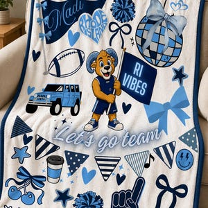 May include: White fleece blanket with blue and navy graphics. Features a cartoon ram mascot holding a flag that says "RI VIBES". Includes a football, jeep, bows, hearts, and the text "Let's go team".