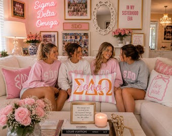 May include: A rectangular throw pillow featuring a white and pink vertical striped pattern with the Greek letters Sigma Delta Omega in orange and the name Ava in pink script lettering centred on the front, displayed on a white sofa.