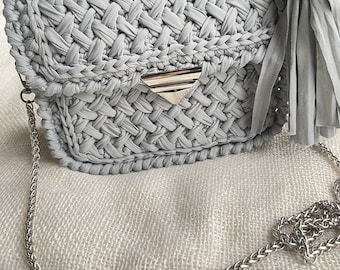 May include: A gray crocheted handbag with a silver chain strap and a tassel with a blue evil eye charm.