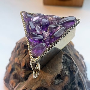 May include: A triangular pendant with a silver frame and a rope-like border. The frame is filled with small, purple amethyst stones.