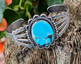 May include: A silver bracelet with a turquoise stone set in a silver bezel. The bracelet has a decorative design with three silver bands and a scalloped edge.