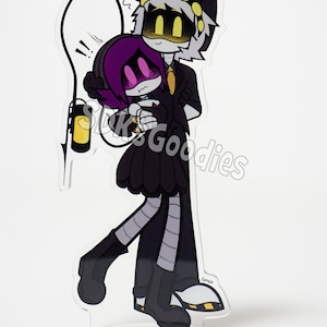 May include: A clear acrylic stand-up featuring a cartoon couple embracing. The characters are in black, white, and purple, with yellow accents. One character wears a black hat and suit, while the other has purple hair and a black dress. A yellow lantern is also included.