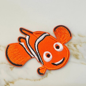 May include: Orange and white embroidered iron-on patch of a cartoon clownfish with a big smile.