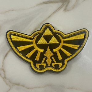 May include: A black and gold embroidered patch featuring the Triforce symbol from the Legend of Zelda video game series.