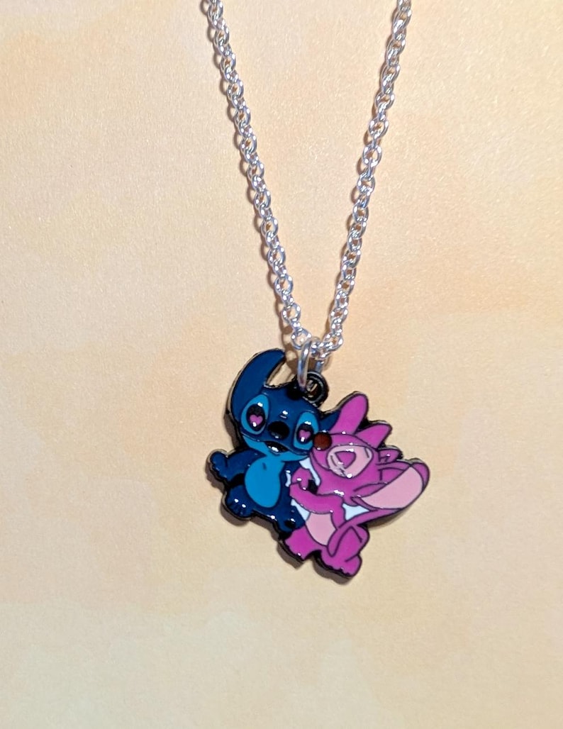 May include: A silver chain necklace with a pendant featuring two cartoon characters. One character is blue, the other is pink. The pendant is approximately 1 inch in height and width.