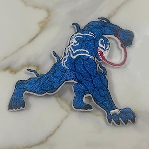 May include: Blue embroidered iron-on patch of a cartoon Venom character with a white outline and a red tongue.