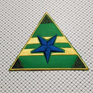 May include: Embroidered patch in a triangular shape. The patch features a green background with a blue star in the center. Gold horizontal stripes and a gold border frame the design. Black triangles are in each corner.
