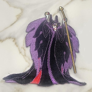 May include: Purple and black embroidered iron-on patch of Maleficent from Disney's Sleeping Beauty. She is wearing a purple and black gown and holding a golden staff.