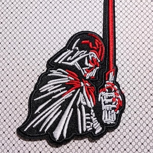 May include: Embroidered patch featuring a stylized depiction of a character in black, red, and white. The character is holding a red lightsaber. The patch has a black border and is set against a patterned background.