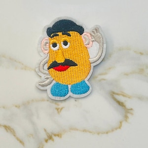 May include: Embroidered iron-on patch featuring a cartoon character with a yellow potato-shaped head, black hair, a black hat, a red mouth, a black mustache, and blue pants.
