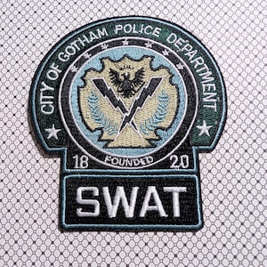 May include: Embroidered patch featuring the text "CITY OF GOTHAM POLICE DEPARTMENT" in a circular design. The patch includes a central emblem with a bird and lightning bolts, and the word "SWAT" below. The patch is green, black, and blue.