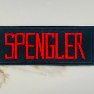 May include: Black embroidered patch with the word "SPENGLER" in red lettering.