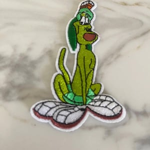 May include: Green cartoon dog with a red nose and a green hat sitting on a white and red butterfly with white wings.