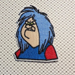 May include: Embroidered patch featuring a cartoon character with blue hair, a tan face, and a blue shirt with red sleeves. The patch has a white border and is set against a patterned background.