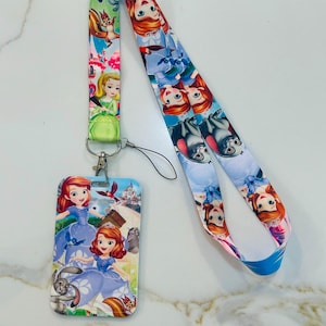 May include: A colorful lanyard with a cartoon image of Disney princesses and a matching ID card holder. The lanyard is blue, pink, and green with a white background. The ID card holder is white with a cartoon image of Disney princesses.