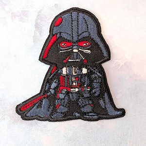 May include: Embroidered patch featuring a cartoon-style Darth Vader. The patch has a black and gray color scheme with red accents on the helmet, eyes, and lightsaber. The design is detailed with stitched lines and shapes, creating a textured appearance.